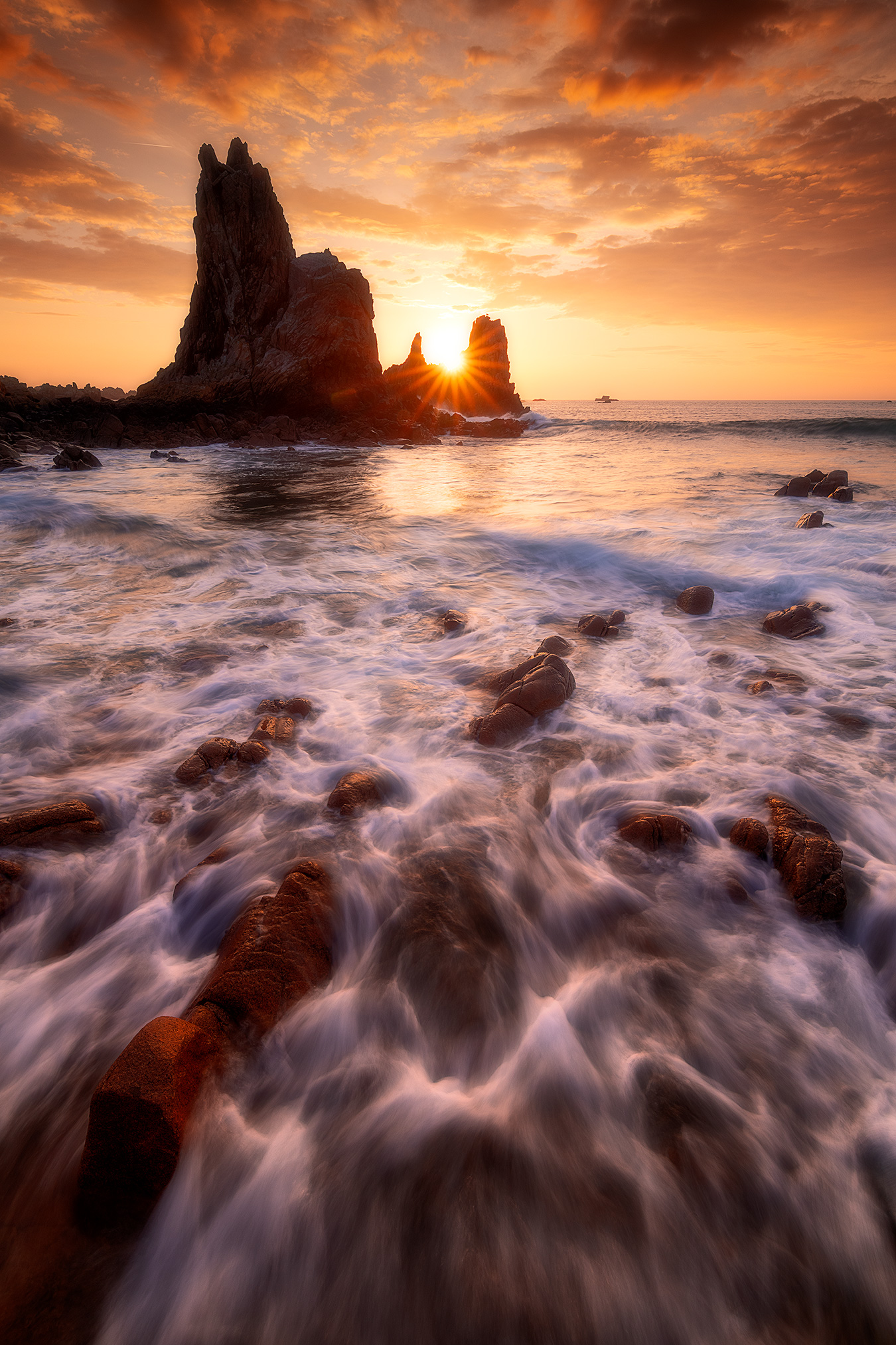 Shiny Pose longue à Pors Scaff sur la côte de granit rose, avec une vague en mouvement au premier plan et un soleil au ras de l’horizon.