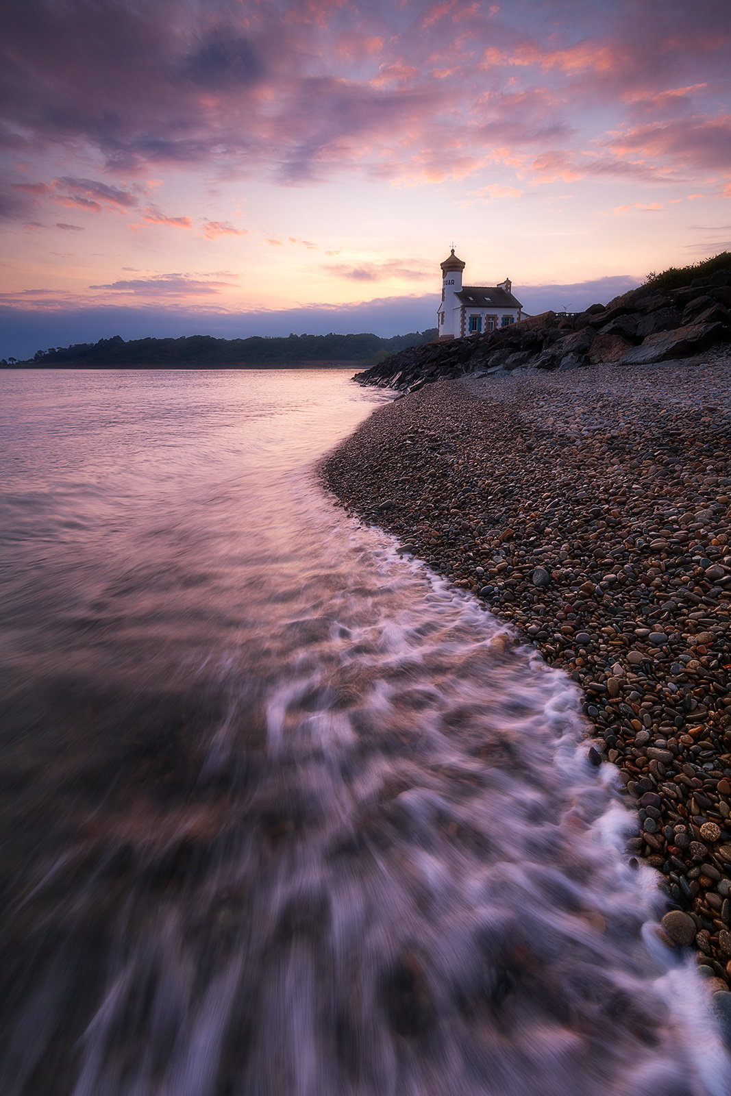 phare de Nantouar Pose longue sur une plage de galets avec le phare de Nantouar à l’heure bleue et une vague en mouvement au premier plan.