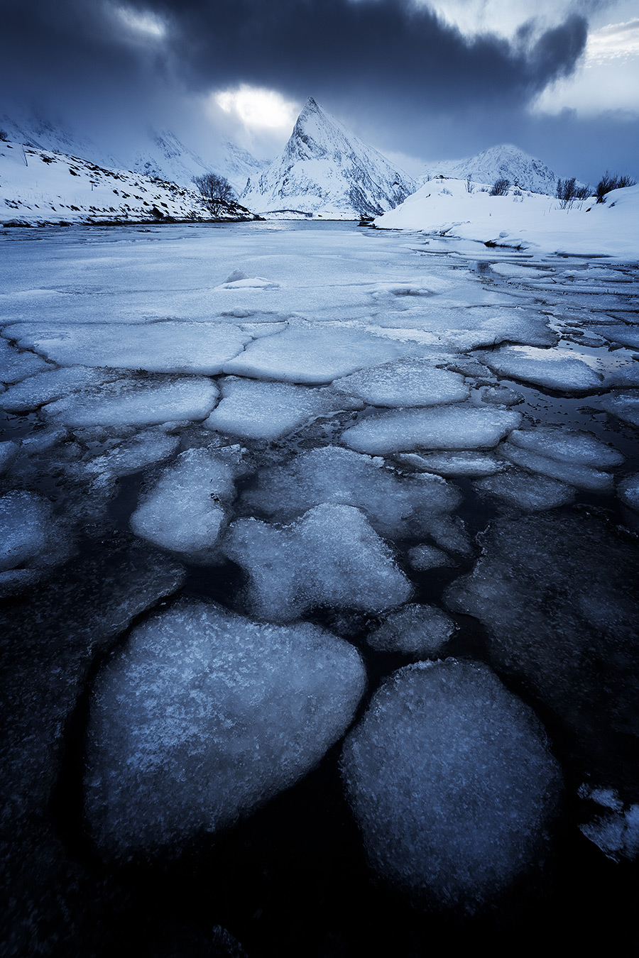 Focus stacking sur des plaques de glace en mouvement Plaques de glace flottant à la surface d'un lac gelé aux Lofoten devant une montagne enneigée.