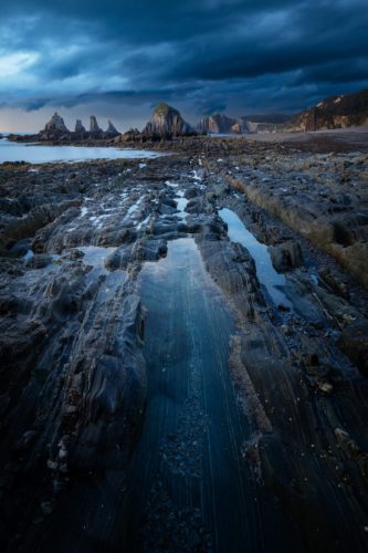 Under Storm. Ambiance de fin du monde sur la plage de Santa Marina, Asturies, Espagne. Formations rocheuses striées sous un ciel orageux, plage de Santa Marina, Asturies, Espagne.