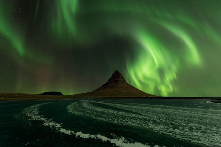 Aurore boréale verte tourbillonnant au-dessus du Kirkjufell, lagune gelée au premier plan, Grundarfjörður, Islande.