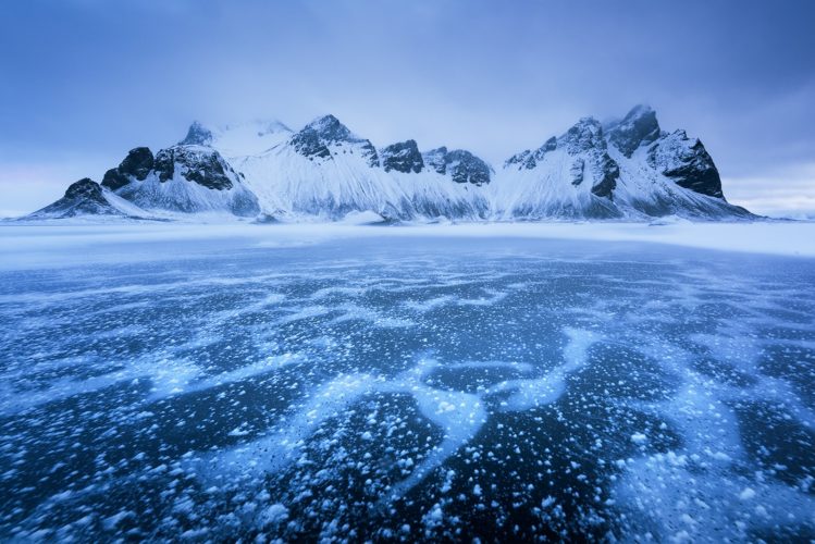 Couche de glace craquelée et parsemée de bulles givrées, le Vestrahorn en arrière-plan, Stokksnes, Höfn, Islande.