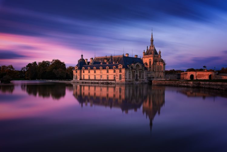 Château de Chantilly au coucher du soleil, reflété dans l'eau, Oise, Hauts-de-France.