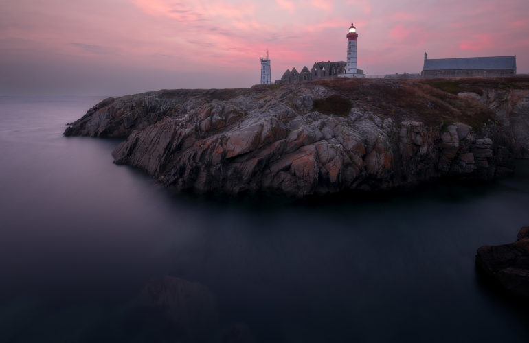 Phare et ruines de l'abbaye de Saint-Mathieu sur une falaise, ciel rose au crépuscule, Bretagne.