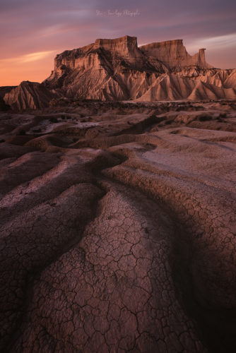 Sol craquelé et falaises érodées au coucher du soleil, désert des Bardenas Reales, Navarre, Espagne.